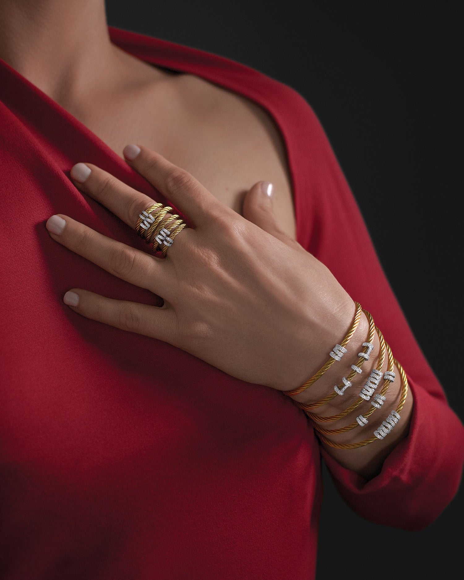 Close-up of a hand wearing multiple gold rings and bracelets on a red garment against a dark background